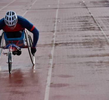 Preparing for wheelchair marathon. Paraplegic male athlete in racing wheelchair warming up alone at outdoor track and field stadium